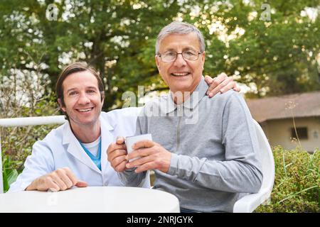 Ritratto di caregiver maschio felice con l'uomo anziano che ha caffè nel giardino di casa di cura Foto Stock
