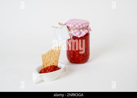 Vasetto di salsa di pomodoro con etichetta vuota e piccolo recipiente con salsa e cracker isolato su fondo bianco Foto Stock
