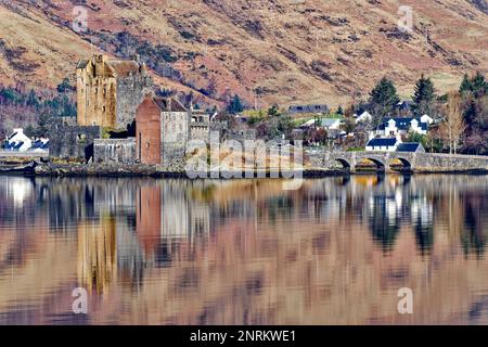 Eilean Donan Castello Loch Duich Scozia il castello e il ponte riflesso nel lago di mare e circondato da case del villaggio di Dornie Foto Stock