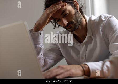 ritratto di un giovane lavoratore seduto davanti al computer. È stanco e stressato e tiene la testa nelle sue mani Foto Stock