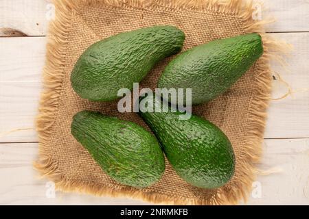 Quattro succulenti avocado con tovagliolo di iuta su un tavolo di legno, macro, vista dall'alto. Foto Stock