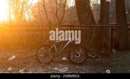 Bicycle gt aggressore si trova vicino alla recinzione con spazzatura scongelata in primavera dalla neve vicino alle pozzanghere al tramonto del giorno sulla strada Foto Stock