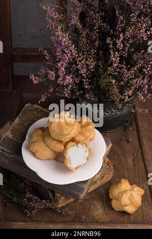 Autunno Vintage Provence Still Life con un gruppo di dolci francesi Crema bianca Eclairs sul piatto, fiori di Heather e vecchi libri. Cemento grigio rustico Ru Foto Stock