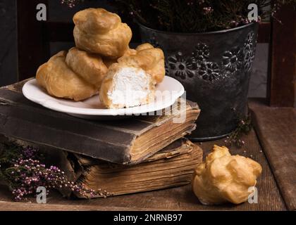 Autunno Vintage Provence Still Life con un gruppo di dolci francesi Crema bianca Eclairs sul piatto, fiori di Heather e vecchi libri. Cemento grigio rustico Ru Foto Stock