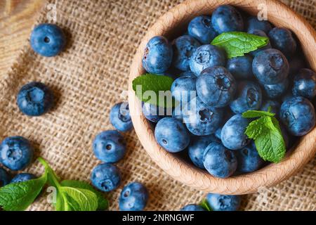 Mirtilli freschi e succosi appena raccolti con foglie di menta verde in ciotola di legno chiaro su tavolo rustico. Mirtillo su tavole orizzontali backgroun in legno Foto Stock