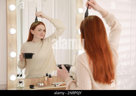 Giovane donna che tintura i capelli con l'henné vicino allo specchio Foto Stock