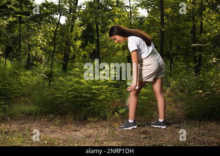 Donna che applica repellente per insetti sulla gamba nel parco. Prevenzione punture di zecca Foto Stock