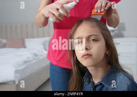 Madre usando nit pettine e spray sui capelli della figlia a casa. Trattamento antighiaccio Foto Stock