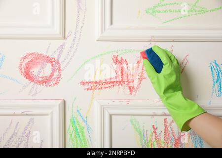 Donna che cancella il disegno del bambino dal muro bianco, primo piano Foto Stock