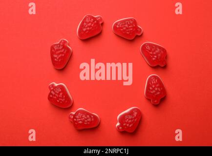 Deliziose caramelle alla fragola gommose su fondo rosso, piatto. Spazio per il testo Foto Stock