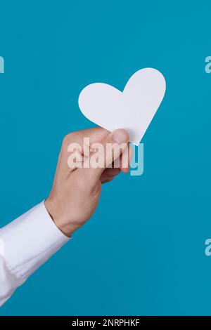 un uomo tiene in mano un cuore bianco davanti a uno sfondo blu Foto Stock
