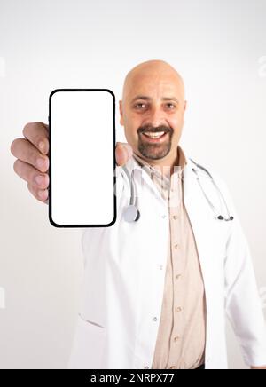 Ritratto di medico allegro che mostra lo schermo vuoto di smartphone per la simulazione. Operaio professionista dell'ospedale millenario caucasico che indossa uniforme bianca. Foto Stock