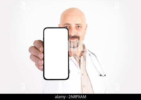 Medico caucasico maschio che mostra smartphone. Grande schermo bianco vuoto per un'immagine da beffa. Sfondo bianco isolato, spazio di copia. Annuncio app mobile ospedale. Foto Stock