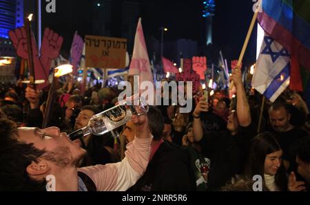 TEL AVIV, ISRAELE - 25 FEBBRAIO: Un manifestante beve una bevanda alcolica Arak durante una manifestazione contro la nuova coalizione di destra del primo ministro israeliano Benjamin Netanyahu e le sue proposte di cambiamenti giudiziari che mirano a indebolire la Corte Suprema del paese il 25 febbraio 2023 a Tel Aviv, Israele. Decine di migliaia di persone si radunano per l'ottava settimana consecutiva in tutto Israele contro l'ampia e controversa riforma del sistema giuridico israeliano. Foto Stock