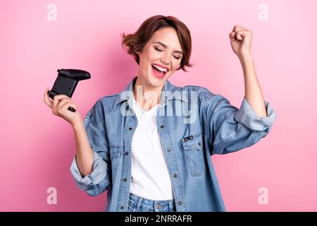 Foto di donna fortunata eccitata indossare jeans camicia vincendo gioco playstation isolato sfondo di colore rosa Foto Stock