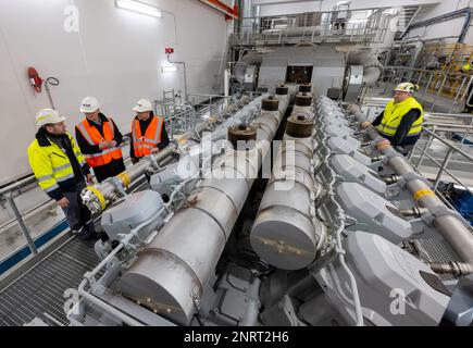 Chemnitz, Germania. 27th Feb, 2023. Wolfram Günther (Verdi, 2nd da destra), Ministro dell'energia in Sassonia, visita l'impianto di cogenerazione dei motori del fornitore di energia eins energie a Chemnitz. Il motivo della sua visita è di discutere i piani attuali per il cambiamento regionale dell'energia, l'espansione delle energie rinnovabili e la questione del futuro approvvigionamento energetico. Credit: Hendrik Schmidt/dpa/Alamy Live News Foto Stock