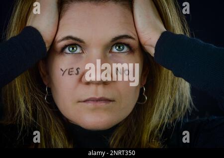 prendere decisioni - ritratto di una bella donna bionda con sì e no scritto sulle guance e in cerca di risposta Foto Stock