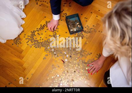 mani umane che raccolgono monete sparse sul pavimento di legno Foto Stock