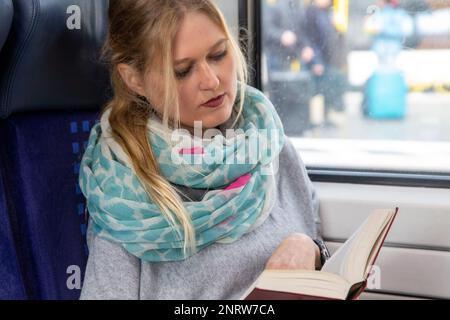 Giovane donna in treno che legge un libro (modello rilasciato) Foto Stock