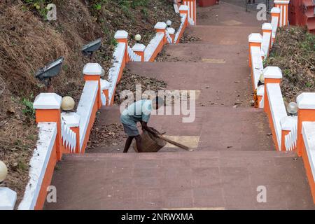 Panjim, Goa, India - Gennaio 2023: Un uomo indiano che scopa una strada con una scopa sulle scale che portano al tempio Maruti a Panaji. Foto Stock