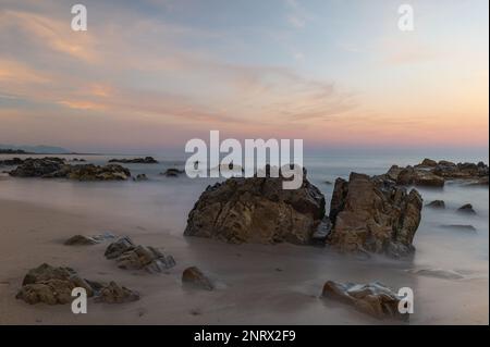 La spiaggia, i rochers et la mer cotonneuse accompagnés d'un beau dégradé de couleurs que laisse le coucher de soleil Foto Stock