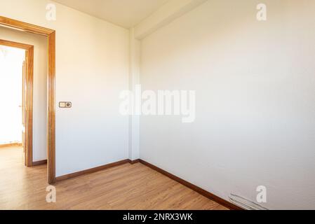 Piccola camera vuota con pavimento in rovere, pareti bianche con gotelet e porta di accesso ad un corridoio di fronte ad un'altra stanza simile Foto Stock