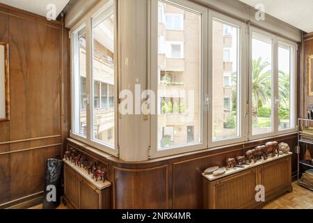 Angolo di una stanza con finestre in alluminio, pareti rivestite in legno con coperture radiatore con ripiani in marmo e figure in legno Foto Stock