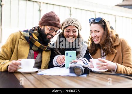 gruppo di tre amici felici utilizzando il telefono in caffè all'aperto il giorno di sole - concetto di vacanze allegre Foto Stock