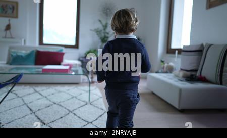 Retro di un ragazzino che corre a casa in casa. Bambino pieno di energia corre in casa moderna appartamento. Piccolo runner per bambini Foto Stock