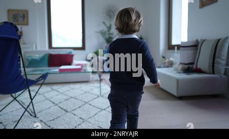 Retro di un ragazzino che corre a casa in casa. Bambino pieno di energia corre in casa moderna appartamento. Piccolo runner per bambini Foto Stock