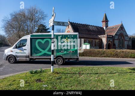 Morrisons supermercato di consegna furgone guida attraverso Rowlands Castle di fronte alla chiesa del villaggio, Hampshire, Inghilterra, Regno Unito Foto Stock