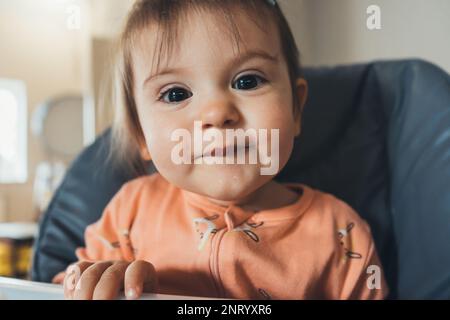 Primo piano ritratto di una bambina seduta su un seggiolone pronto a mangiare. Stile di vita quotidiano. Foto Stock