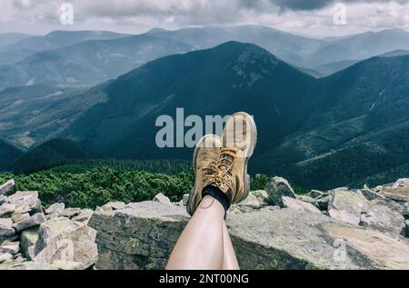 Piedi Donna scarpe da trekking relax all'aperto Viaggi giovane donna gambe shod in stivali all'aperto. Concetto di stile di vita montagne sullo sfondo Vacanze estive. Foto Stock