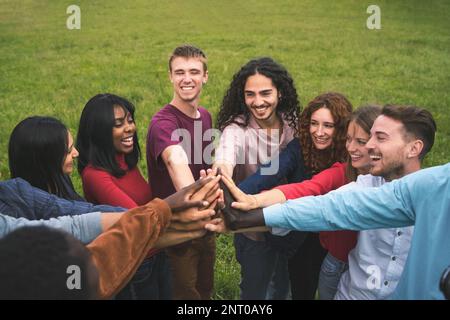 Vista dall'alto verso il basso di un gruppo multirazziale di giovani amici che si uniscono con gioia in un alto cerchio all'aperto. Lo sfondo del campo d'erba crea un blan Foto Stock