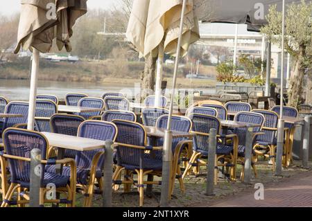 Terrazza vuota con sedie in vimini blu e tavoli grigi con un piccolo lago sullo sfondo Foto Stock