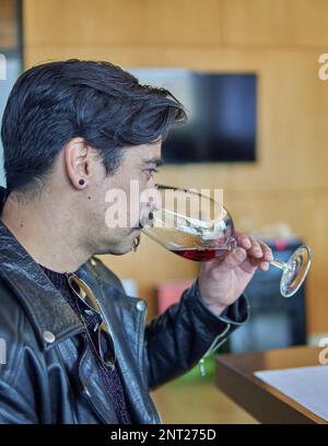 l'uomo latino in profilo ad una degustazione di vino in una cantina in mendoza argentina. Uomo brunetta in giacca di pelle con baffi che tiene e odora un bicchiere di Foto Stock