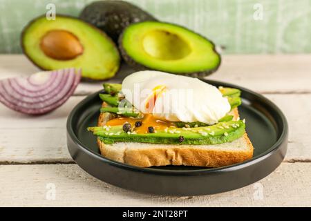 Piatto con delizioso toast all'avocado e uovo in camicia su fondo di legno bianco Foto Stock