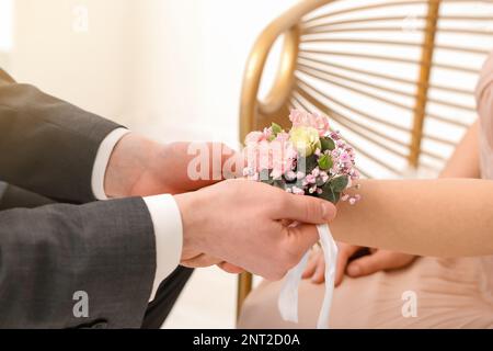 Giovane uomo che legava il corsage intorno al polso del suo appuntamento, primo piano Foto Stock