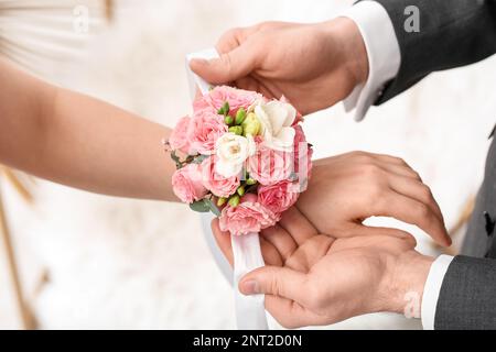 Giovane uomo che legava il corsage intorno al polso del suo appuntamento, primo piano Foto Stock