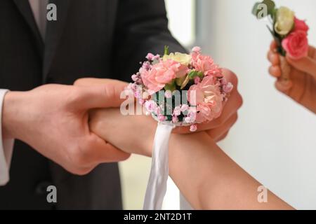 Giovane uomo che legava il corsage intorno al polso del suo appuntamento, primo piano Foto Stock