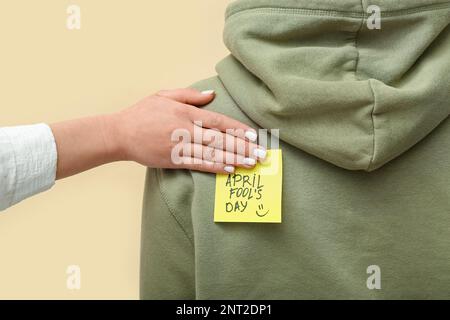 Donna che si attacca carta con testo APRILE FOOL's GIORNO sulla schiena dell'amico contro sfondo a colori, primo piano Foto Stock