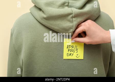 Donna che si attacca carta con testo APRILE FOOL's GIORNO sulla schiena dell'amico contro sfondo a colori, primo piano Foto Stock