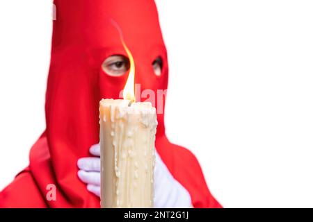 La candela in fiamma di un giovane Nazareno con un cappuccio rosso che fa la sua stazione di penitenza nella processione della settimana Santa. Fuoco selettivo solo con fiamma candela Foto Stock