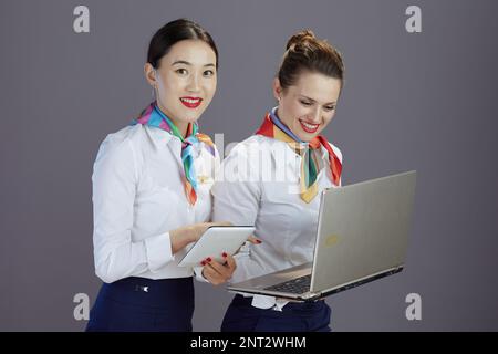 Donna moderna e sorridente, con gonna blu, camicia bianca e sciarpa con notebook e tablet PC isolati sul grigio. Foto Stock