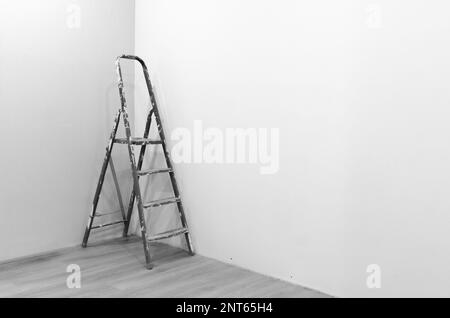 Fotografia in bianco e nero di una scala per riparare una vernice bianca macchiata in piedi nell'angolo di una stanza appena dipinta sul nuovo piano. Foto Stock