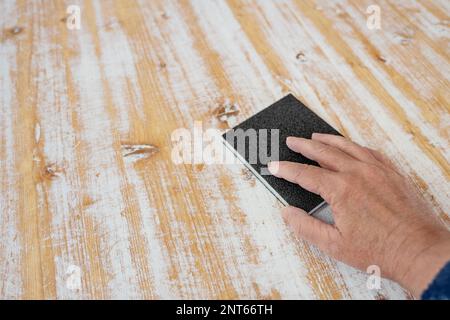 Mano con una spugna abrasiva che rimuove la vernice bianca dalla superficie di legno di un grande tavolo, ristrutturazione di mobili fatti in casa, spazio copia, fuoco selezionato, n Foto Stock