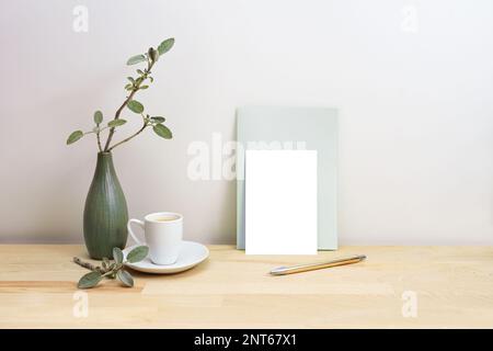 Biglietto d'auguri vuoto o mock-up invito con una penna accanto a un vaso verde grigio con rami salvia e una tazza di caffè, semplice stile arredamento casa, copia spac Foto Stock