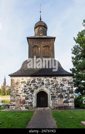 Piccola fieldstone e cappella in legno presso la chiesa di San Sigfrid e mattoni rossi costruirono sullo sfondo la chiesa di Sipoo, Sipoo, Finlandia. Foto Stock