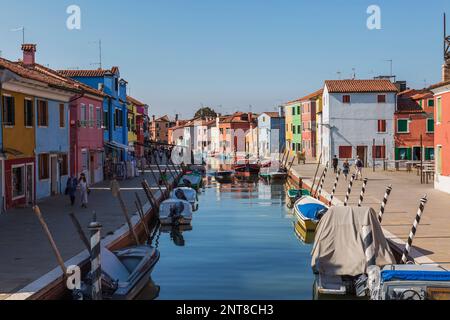 Barche ormeggiate sul canale fiancheggiato da case di stucco colorate, negozi e turisti, Isola di Burano, Laguna di Venezia, Venezia, Veneto, Italia. Foto Stock