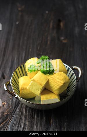 Tofu morbido giallo su sfondo tavolo di legno, taglio cubo Foto Stock